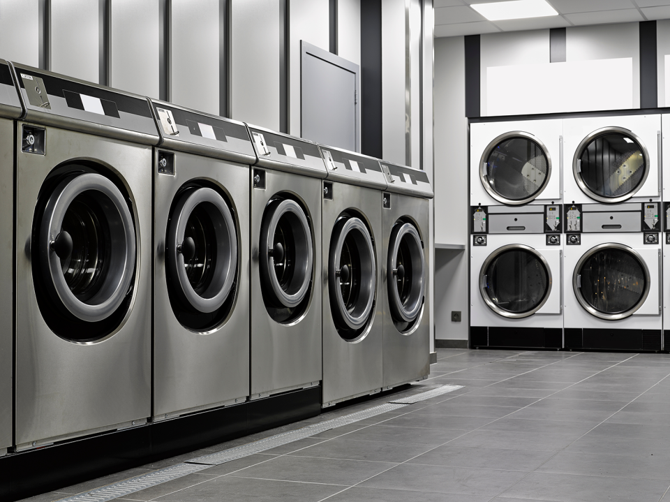 Top load washers in a laundry mat next to front load stacked washing machines.